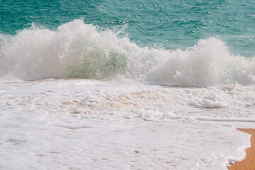 Turquoise waves with white foam on the banks of benagil beach in portugal.