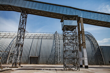 Metal Hangar and transporter. Standard Cement plant clinker warehouse. Blue sky with clouds.