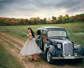 Young beautiful happy retro woman near the old car. Attractive elegant lady in vintage white polka...