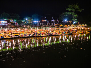 Fototapeta premium Beautiful view of nam song river with Tourist on riverside restaurant and the mountain in the night at Vangvieng city Lao.Vangvieng City The famous holiday destination town in Lao.