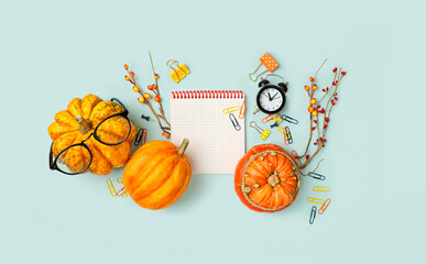autumn composition with notepad, pumpkin, alarm clock on blue background. fall time concept. flat lay.  copy space