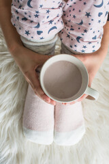 Girl hands hold cup of hot coffee at home. Top and closeup view on hands and legs in warm kntitted long socks. Winter and stay at home concept with copy space.