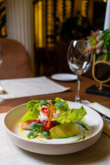 Salad with crab and avocado on a dark background. Arugula salad leaves seasoned with sauce on white wine with crab meat and grilled avocado in soft focus. Top view