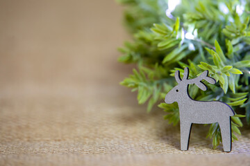close-up of one isolated wooden white reindeer and green wreath with lights on jute background, christmas decoration with branch and deer, front view