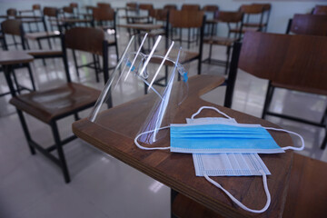 The medical blue mask and face shield on the wood lecture chairs place distancing in the empty classroom. Concept during the germs, coronavirus disease covid-19 outbreak. Back to school concept.