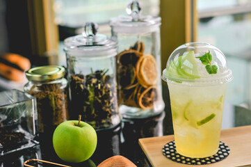 A Signature cold drink Green apple Juice decorated with fresh apple slide and mint leaf in a plastic takeaway cup 