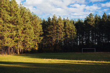 Naklejka premium A football field in the middle of a forest with a white soccer goal in the sun.