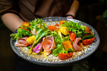 Female hands holding hydroponic vegetable bacon salad with wooden table background.