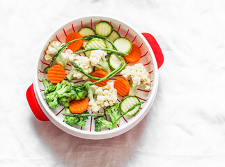 Cooking healthy food concept. Fresh vegetables broccoli, zucchini, carrots, asparagus in a steamer on a light background, top view