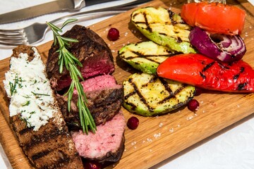 Amazing medium fried  juicy filet mignon with fried vegetables, slice of toasted crusty ciabatta bread and  rosemary on wooden tray. Restaurant.