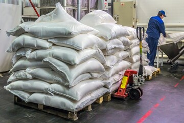 Many white bags of sugar in a pile and a man in a uniform at the confectionary.