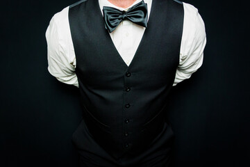 Portrait of Man in Black Vest and Bow Tie with His Hand Behind His Back. At Your Service. Copy Space for Service. Concept of Service Industry and Professional Hospitality