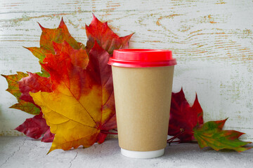 Coffee cardboard cup with a red lid on background of autumn maple leaves yellow, red, green color