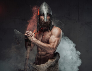 Nord warrior with muscular build and helmet on him standing with two handed axe in smoky dark...