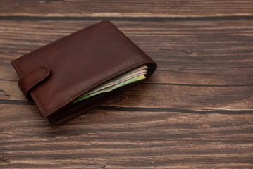 Closed men's brown wallet on a wooden brown background with money. Close-up