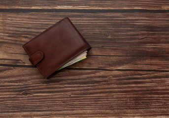 Closed men's brown wallet on a wooden brown background with money. Close-up from above