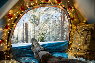A man lying in a tent decorated with Christmas lights wearing warm wooden. Beautiful winter wild...