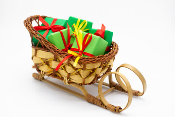 Old-fashioned wicker Santa sleigh with Christmas gifts wrapped in green paper with red ribbon