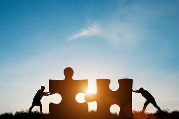 Silhouette two men pushing to connect jigsaw puzzle with sunlight and blue sky. It is symbol of business corporate teamwork to  solutions, success and strategy concept.