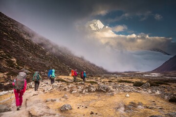 Group of trekkers walk along Khumbu valley. Ama Dablam mountain (6812m) covered with snow and light clouds is on the background. Nepalese Himalayas.