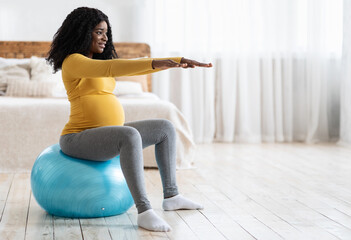 Black expecting woman training on ball, getting ready for childbirth