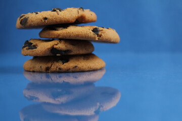 a round cookie with chocolate drops is stacked on top of each other on a blue bright saturated background with a reflection side view of copy space