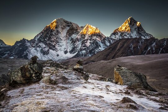 Taboche (6,495m) and Cholatse (6,440m) mountains in early morning which peaks lightened with sun beams. Big rocks are on the foreground. The Himalaya mountains. Nepal.