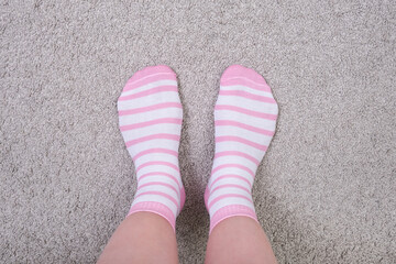 Woman female legs wearing pink and white striped plain cotton socks of classic style with elastic band standing on a cozy carpet at home