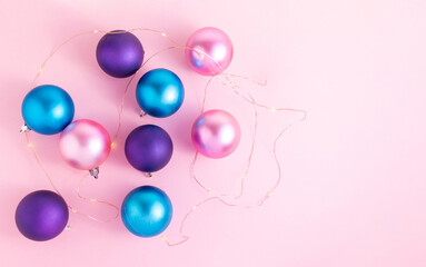 Pink, turquoise and purple satin Christmas balls on a pink background with small lights around them. Christmas decoration for ideal for the New Year's Eve and New Year