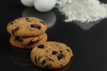 kitchen still life cooking process homemade chocolate cookies with chocolate drops in the background flour and chicken eggs lie on a black mirror background with a reflection of copy space