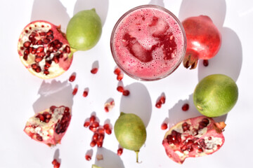 open pomegranates, seeds, glass of pomegranate juice and lemons on white background. Top view.