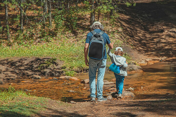 Father and son cross stream in forest. Man and child with backpacks on background of forest. Travel concept with children. Life style