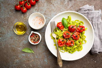 Green Tagliatelle pasta with cherry tomatoes and basil on gray background, top view