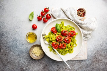 Green Tagliatelle pasta with cherry tomatoes and basil on gray background, top view