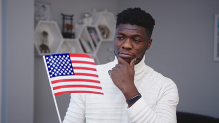 Young thoughtful black man holding usa flag. Asylum seeker thinking about job opportunities in USA....