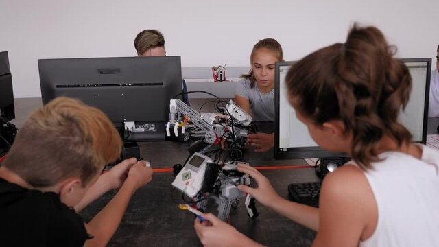 Group of children are making robots from the constructor at the desk with computer in the School of Robotics.