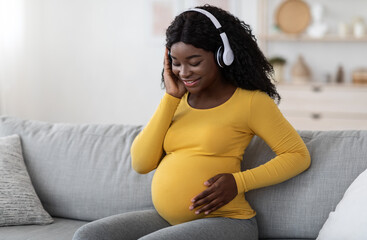 Happy pregnant black woman listening to music in headphones