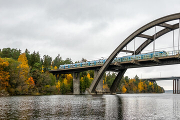 Nature autumn landscape scene with large arch concrete bridge with train crossing over calm water.