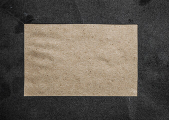 An overhead photo mockup of a square brown kraft card on a black texture, with a place for text. Top view