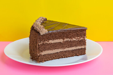 a piece of chocolate cake on white plate on pink and yellow background