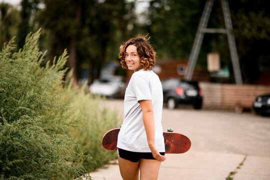 Young Cheerful Woman In White T-shirt With Her Head Turned Back And Skateboard In Her Hand