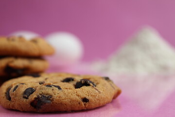 kitchen cooking process homemade chocolate cookies with chocolate drops in the background flour and chicken eggs lie on a pink fuchsia mirror background with a reflection of copy space