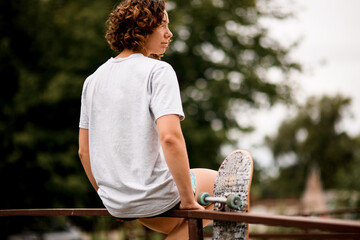 Rear view of young woman who sits on wooden railing and skateboard nearby. © fesenko