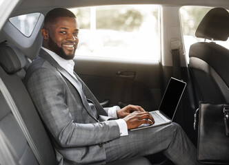 Smiling black guy businessman working on laptop with blank screen
