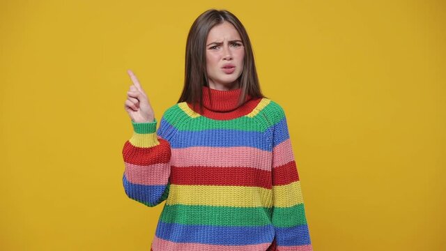 Displeased young woman 20s in colorful sweater posing isolated on yellow background studio. People lifestyle concept. Looking camera say no showing stop gesture with crossed hands showing thumb down