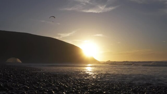 Paragliding freedom flight over Legzira Beach in Morocco evening sunset over ocean coast with rocks and peaceful sunny landscape
