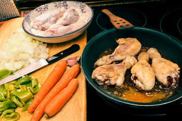 preparing floured and fried chicken thighs in a frying pan with vegetables