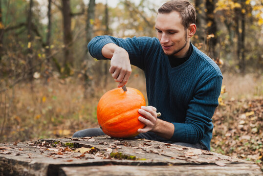 A young man carves the face of a pumpkin in out door,