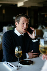 Handsome businessman dressed in the suit drinking wine. Businessman talking to the phone.