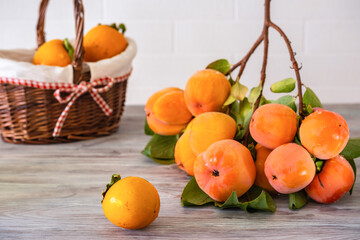 A branch of ripe persimmons on a wooden table against a background of a white brick wall